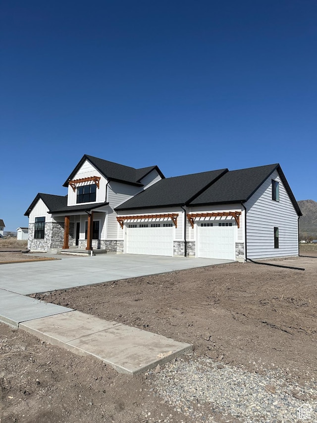 modern farmhouse with concrete driveway, stone siding, and a garage
