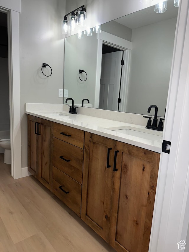 full bathroom with double vanity, a sink, toilet, and wood finished floors
