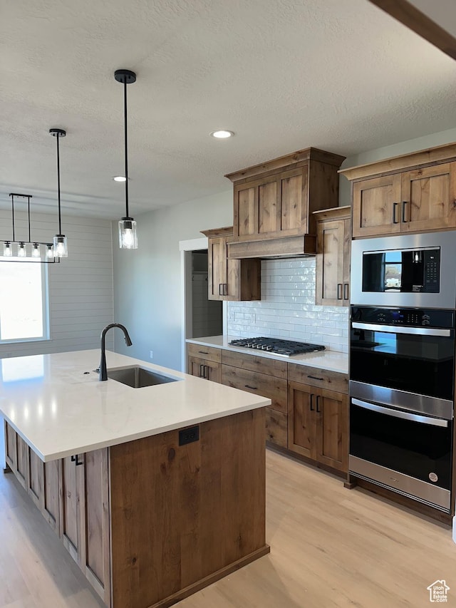 kitchen featuring tasteful backsplash, light wood-style floors, appliances with stainless steel finishes, and a sink