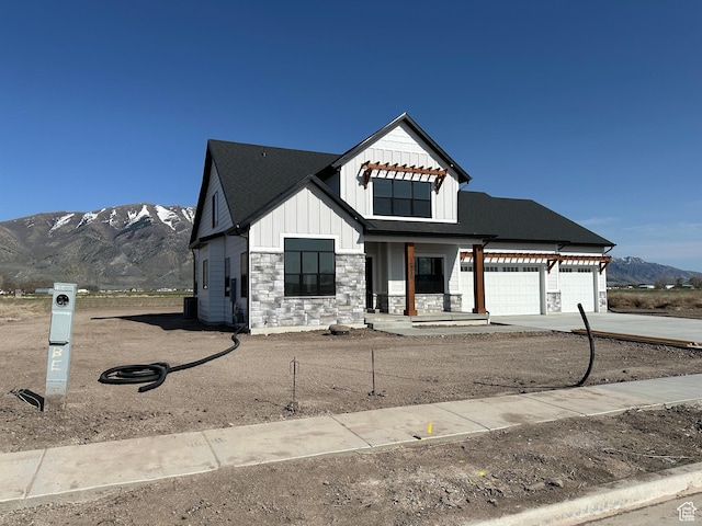 modern farmhouse featuring board and batten siding, a garage, stone siding, a mountain view, and driveway