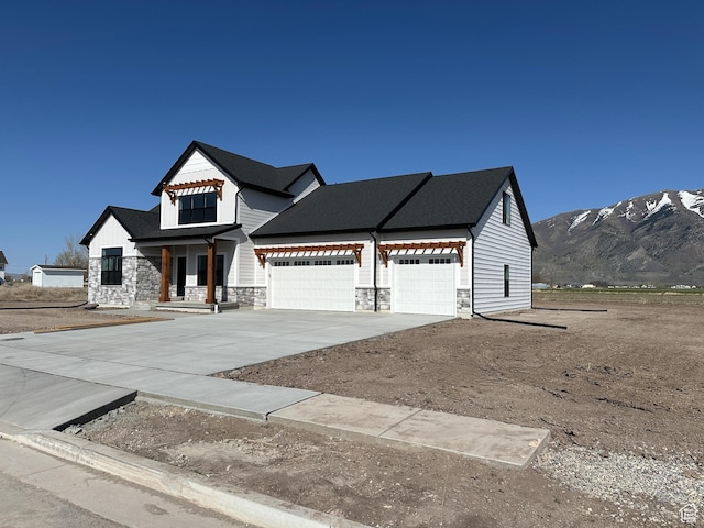 modern farmhouse style home featuring a mountain view, concrete driveway, a garage, and stone siding