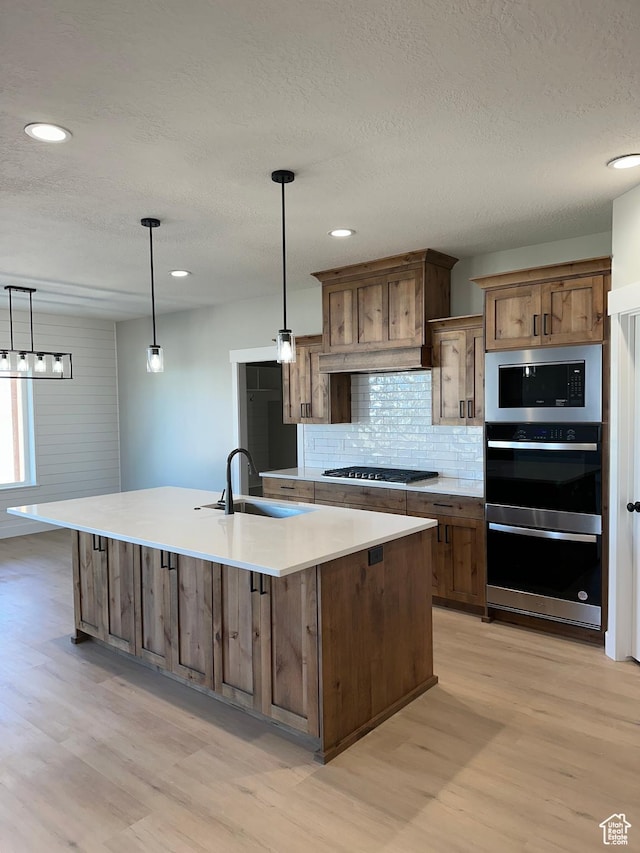 kitchen with light wood-style floors, a large island, a sink, stainless steel appliances, and decorative backsplash