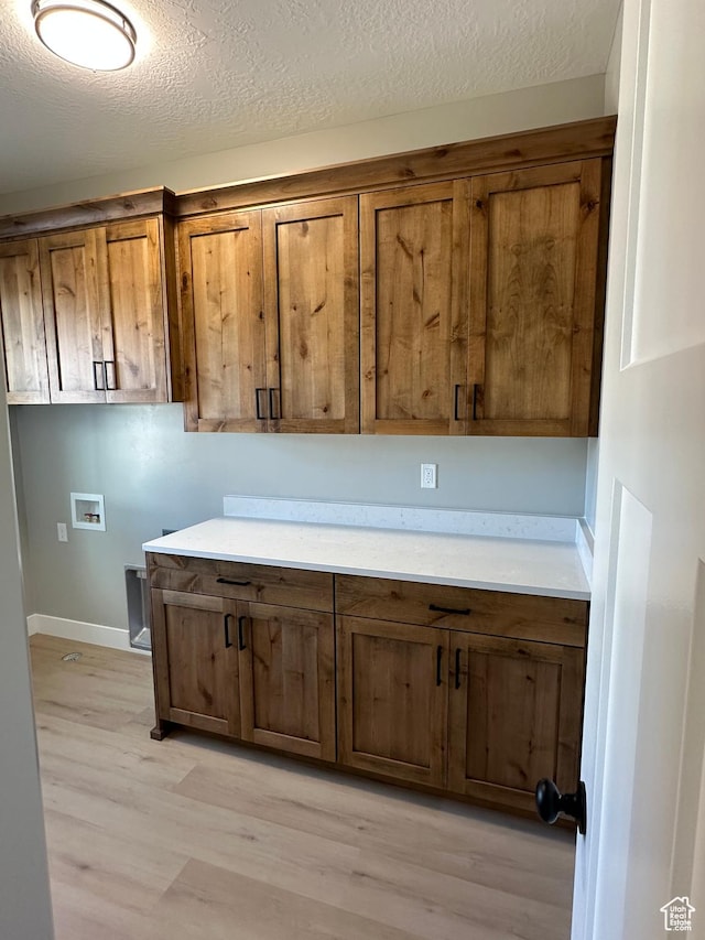 laundry area featuring light wood-style flooring, a textured ceiling, washer hookup, and cabinet space