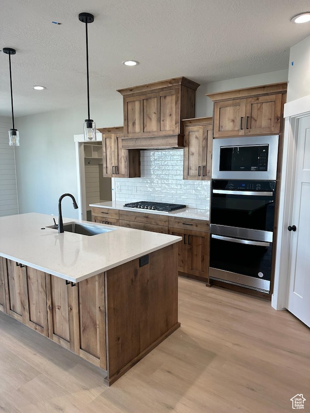 kitchen with stainless steel double oven, gas stovetop, a sink, light wood finished floors, and backsplash