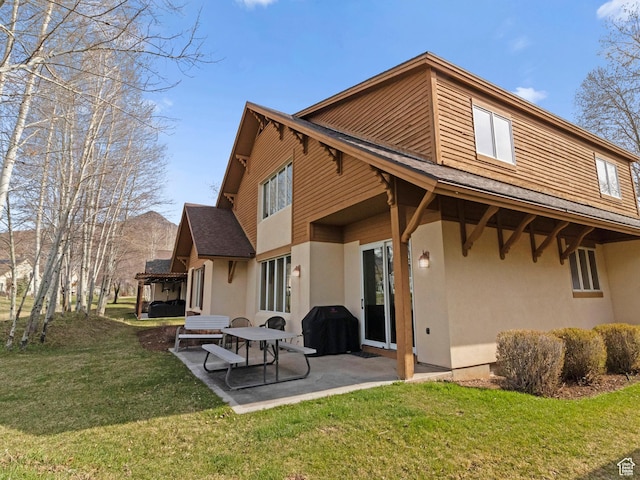 back of property with a patio, a shingled roof, stucco siding, and a yard