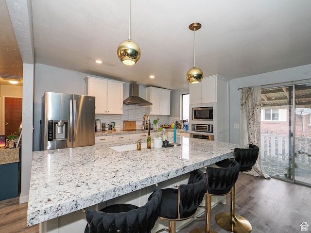 kitchen featuring white cabinets, wall chimney exhaust hood, appliances with stainless steel finishes, wood finished floors, and decorative backsplash