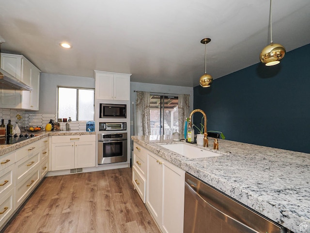 kitchen with white cabinetry, a sink, hanging light fixtures, stainless steel appliances, and light wood finished floors