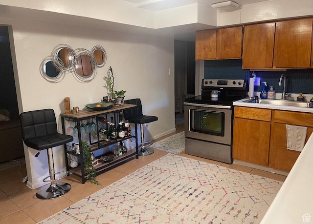 kitchen with brown cabinetry, light tile patterned floors, a sink, and electric stove