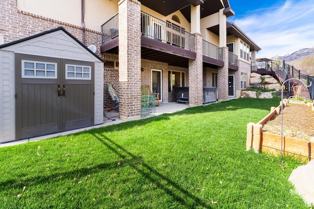 exterior space with a storage unit, brick siding, a patio area, an outdoor structure, and a yard