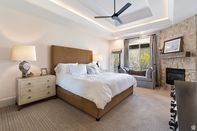 bedroom with a stone fireplace, a tray ceiling, ornamental molding, carpet flooring, and access to exterior