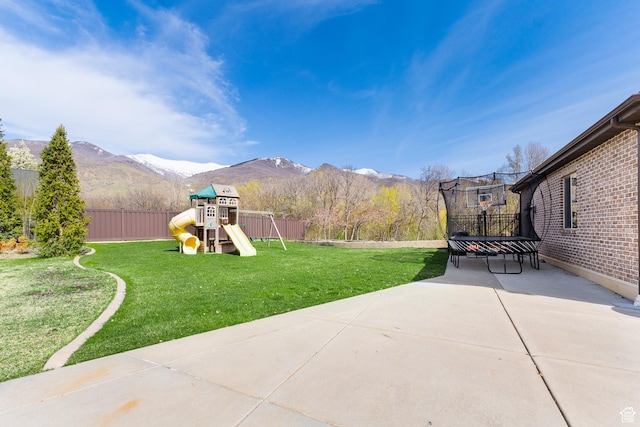 view of yard with a trampoline, a playground, a fenced backyard, a mountain view, and a patio