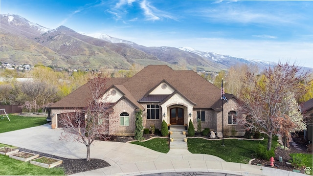 view of front facade featuring brick siding, a front lawn, concrete driveway, and a mountain view
