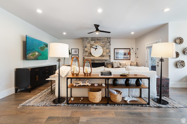 living room with dark wood-style flooring, a ceiling fan, a stone fireplace, and recessed lighting