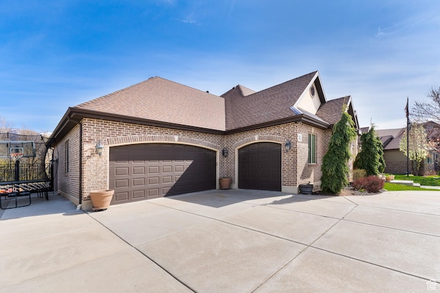 view of side of home featuring brick siding, driveway, a shingled roof, and a garage