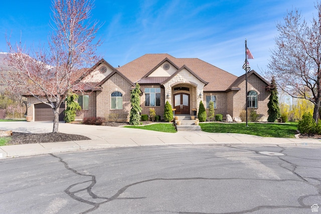 french country style house featuring an attached garage, french doors, driveway, and brick siding
