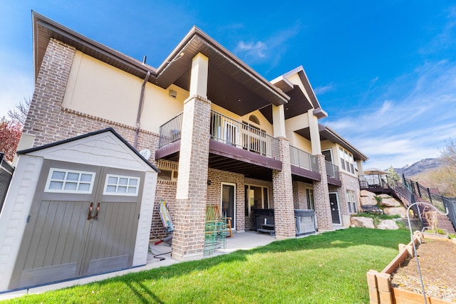 rear view of property featuring a storage shed, a lawn, a balcony, an outdoor structure, and a patio