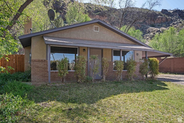 bungalow-style house featuring stucco siding, fence, a front lawn, and brick siding