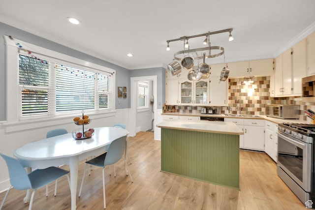 kitchen with stainless steel range with gas stovetop, ornamental molding, light countertops, a wainscoted wall, and a kitchen island