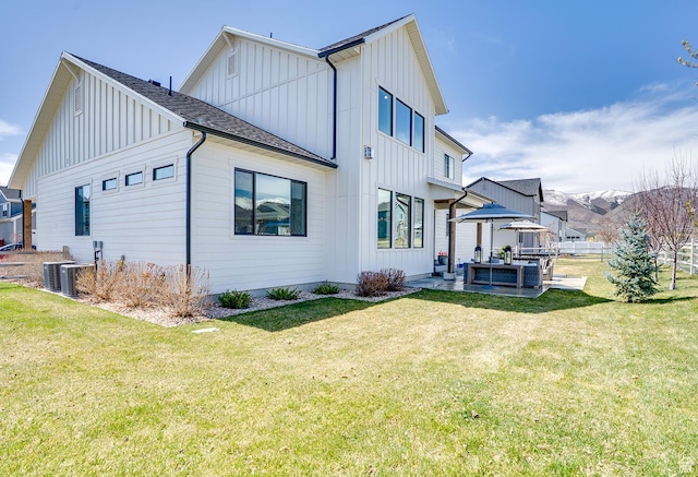 rear view of house with a patio area, a yard, board and batten siding, and fence