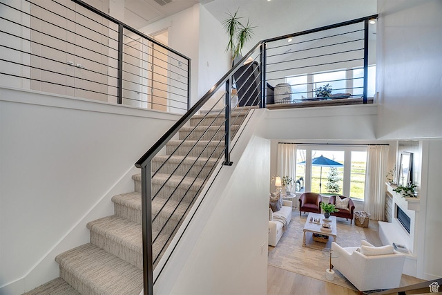 stairway with wood finished floors, a glass covered fireplace, and a towering ceiling