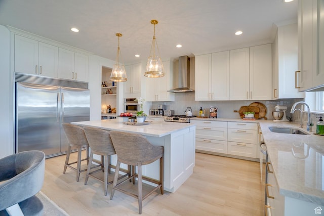 kitchen featuring stainless steel appliances, recessed lighting, wall chimney exhaust hood, and a sink