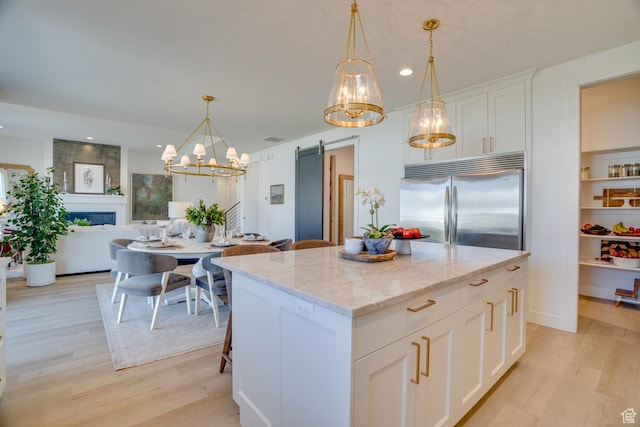 kitchen with built in refrigerator, light wood-type flooring, a chandelier, recessed lighting, and a kitchen island