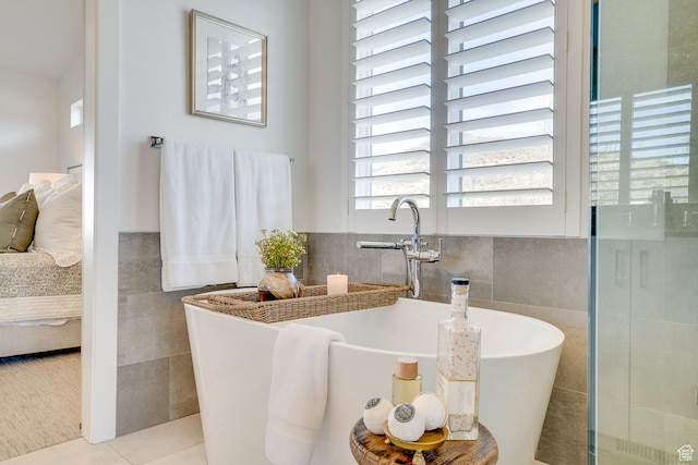 ensuite bathroom featuring ensuite bathroom, tile walls, a freestanding bath, and tile patterned flooring