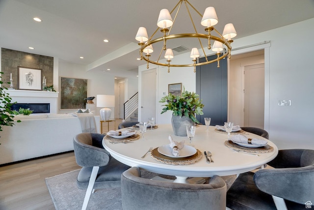 dining room featuring a notable chandelier, a fireplace, stairway, visible vents, and light wood finished floors