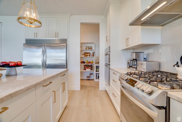 kitchen with wall chimney range hood, white cabinets, appliances with stainless steel finishes, light wood finished floors, and backsplash