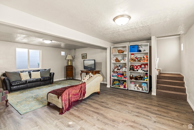living area with stairs, a textured ceiling, baseboards, and wood finished floors