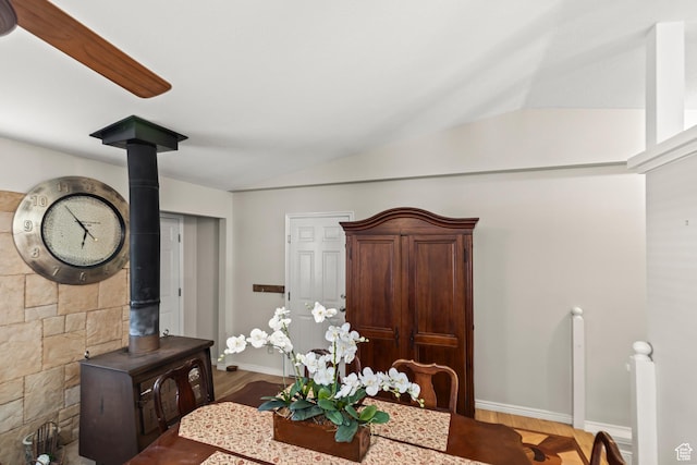 dining room with wood finished floors, a wood stove, baseboards, and lofted ceiling