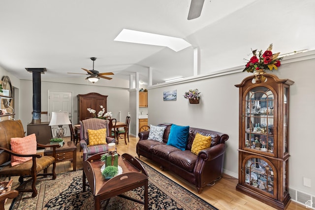living area with baseboards, a wood stove, visible vents, ceiling fan, and light wood finished floors