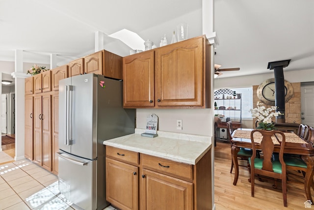 kitchen featuring light wood-style floors, freestanding refrigerator, ceiling fan, a wood stove, and light countertops