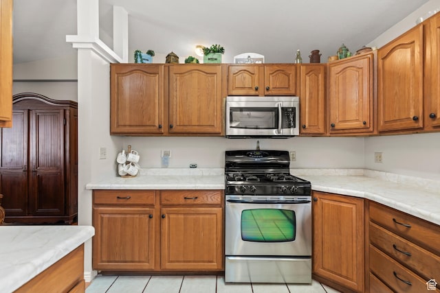 kitchen featuring brown cabinets, light tile patterned floors, light countertops, and stainless steel appliances