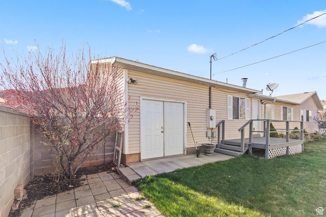 rear view of house featuring a wooden deck, fence, and a lawn