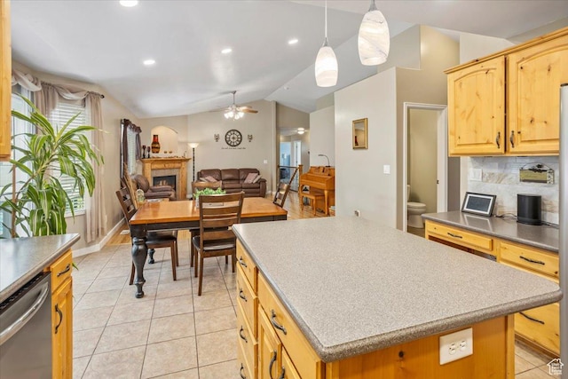 kitchen with light tile patterned floors, dishwasher, a fireplace, vaulted ceiling, and a kitchen island