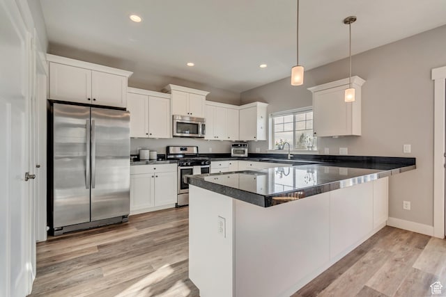 kitchen with a peninsula, light wood-style flooring, white cabinetry, dark countertops, and stainless steel appliances