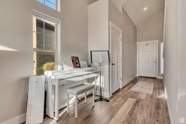 corridor with wood finished floors, high vaulted ceiling, and baseboards