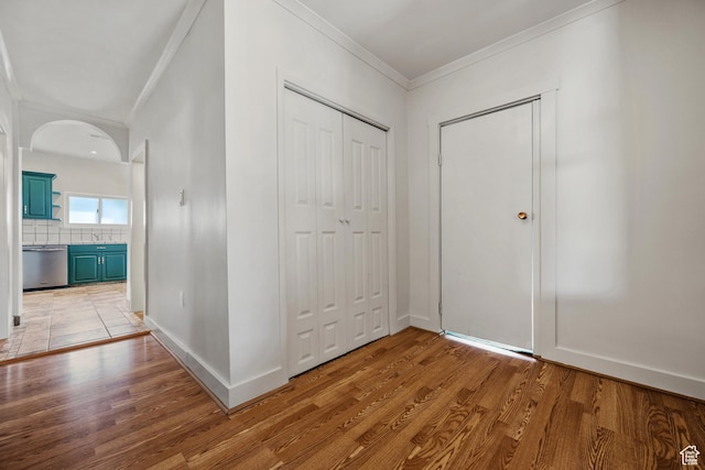 entrance foyer featuring crown molding, baseboards, light wood-type flooring, and arched walkways