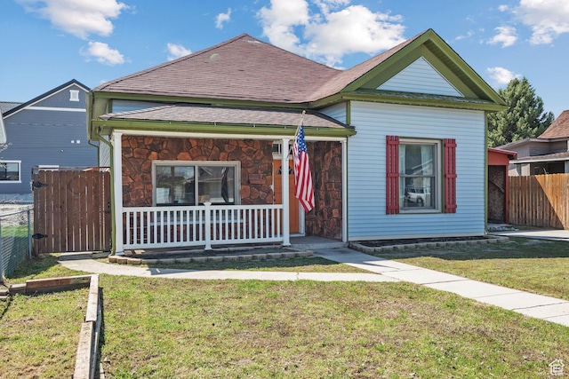 bungalow with covered porch, a front yard, and stone siding