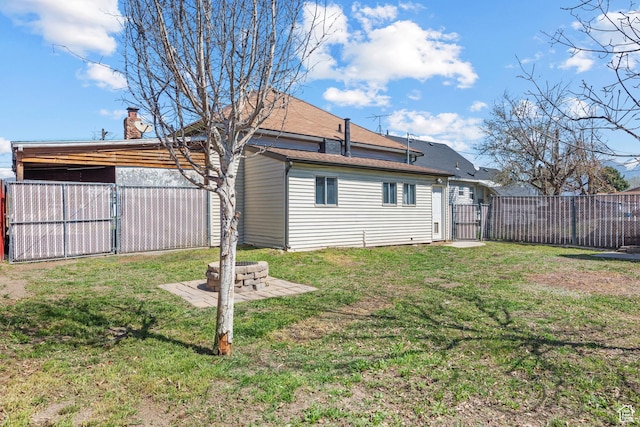 back of house with an outdoor fire pit, a gate, fence, and a lawn
