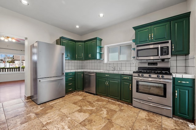 kitchen featuring green cabinets, tile counters, backsplash, and stainless steel appliances