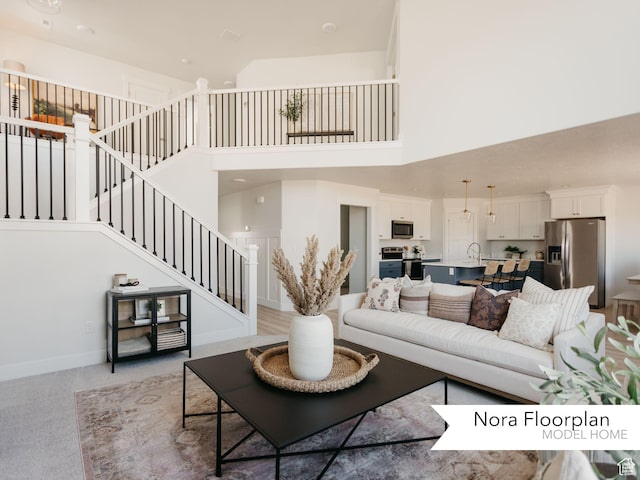 living room with baseboards, light colored carpet, a towering ceiling, and stairs