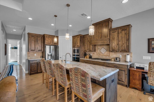 kitchen with tasteful backsplash, light wood-type flooring, visible vents, stainless steel appliances, and a center island with sink