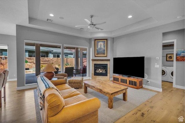 living area with a ceiling fan, visible vents, a tray ceiling, light wood finished floors, and washing machine and clothes dryer