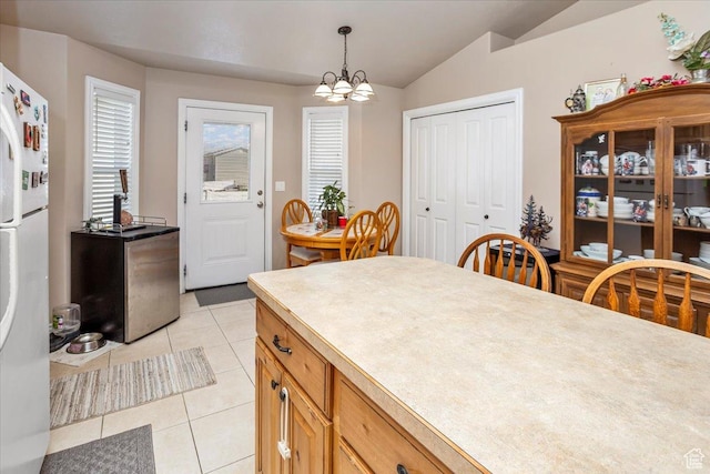 interior space featuring a notable chandelier, light tile patterned floors, freestanding refrigerator, lofted ceiling, and hanging light fixtures