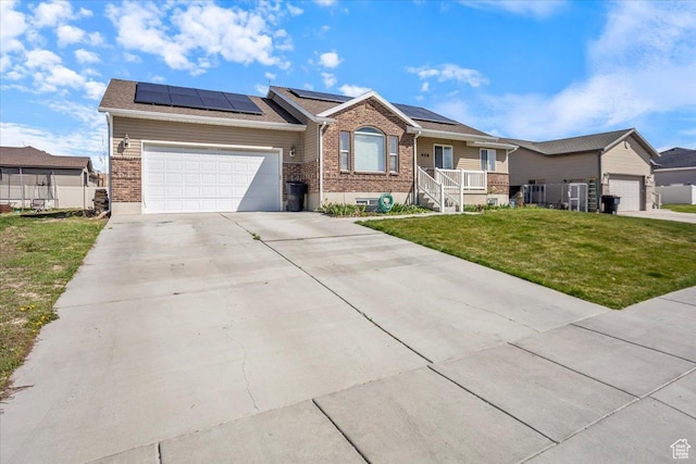ranch-style home with roof mounted solar panels, a front yard, brick siding, a garage, and concrete driveway
