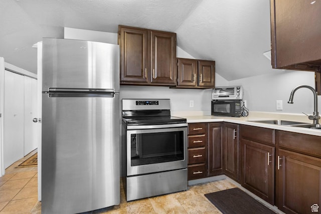 kitchen featuring dark brown cabinetry, vaulted ceiling, light countertops, stainless steel appliances, and a sink