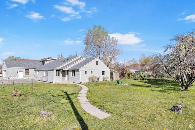 rear view of property featuring a yard, a shingled roof, fence, and a patio area
