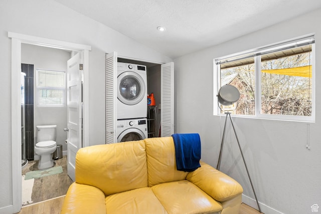 sitting room with lofted ceiling, stacked washer / drying machine, baseboards, and wood finished floors